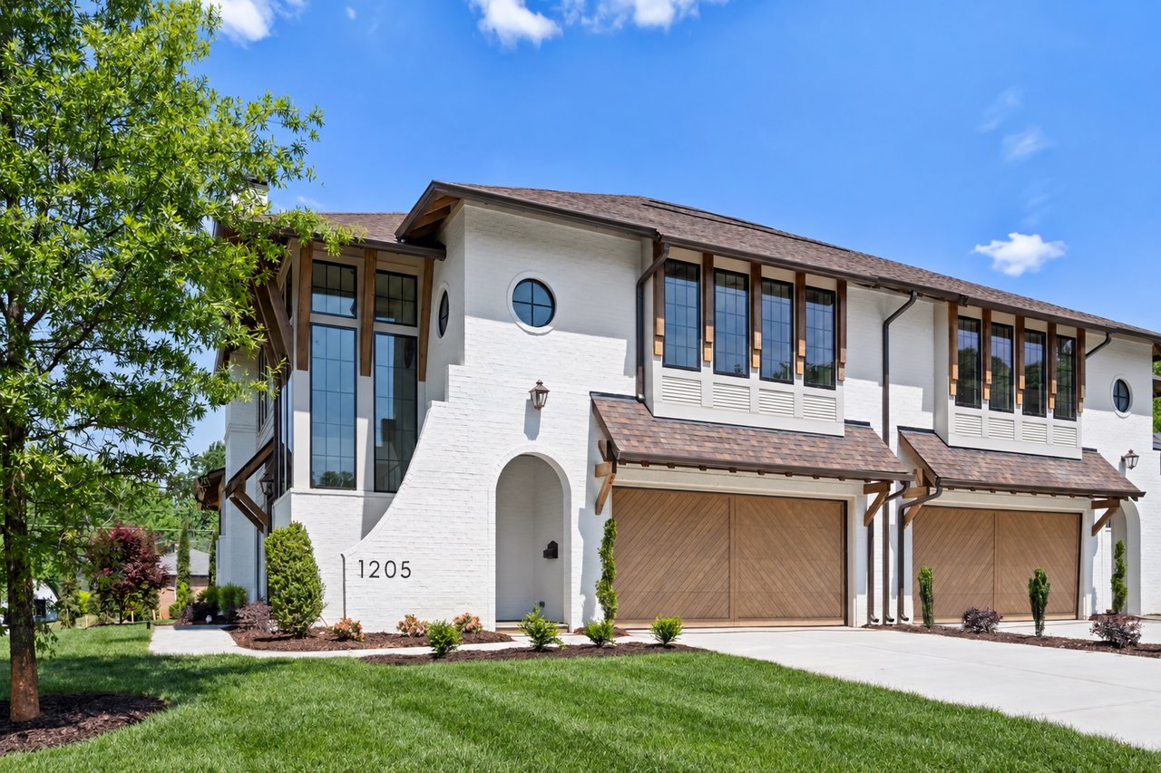 White-brick home at 1205 Jersey Ln with tall windows, wood accents, and double garage doors.
