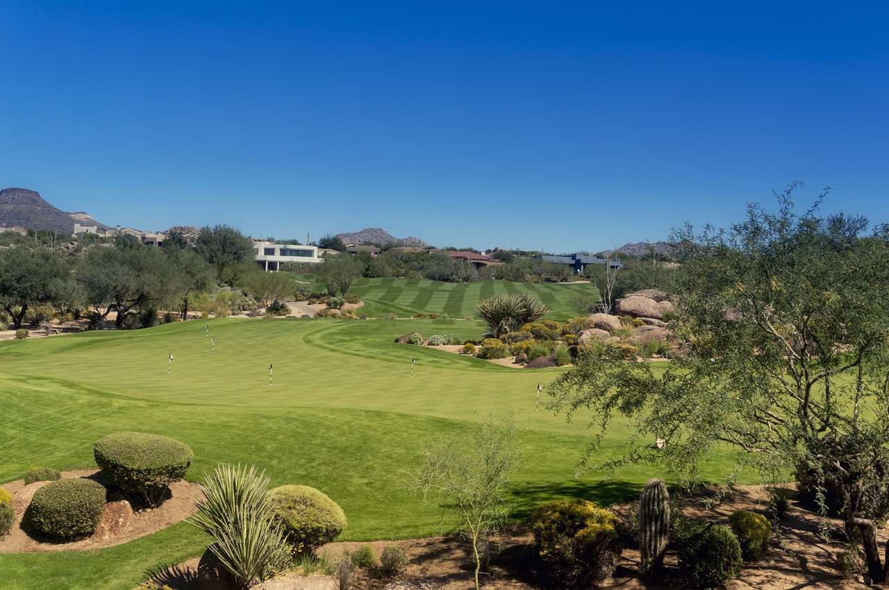 Golf course with manicured putting greens, desert landscaping, and mountains in the distance.