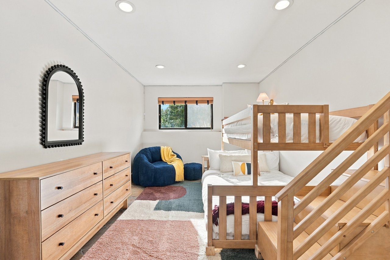 Bedroom with a wooden bunk bed and staircase, a blue chair, and a light wood dresser.