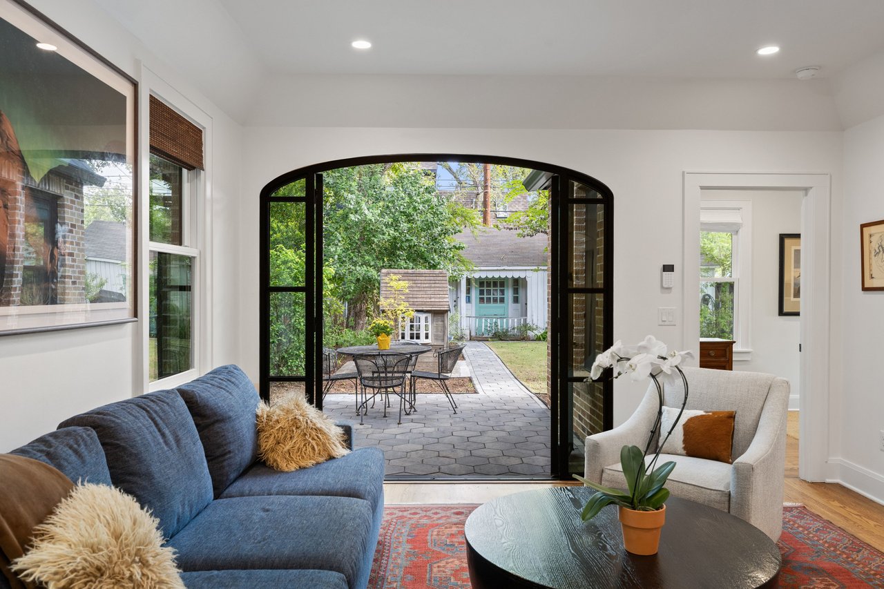 Living room with a blue sofa and cream armchair overlooking a paved patio through an arched doorway.