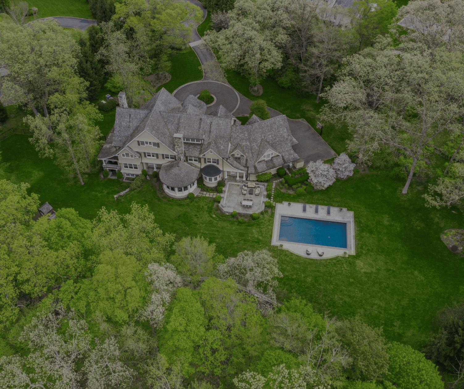 Aerial view of a luxury mid-country Greenwich CT estate with pool and circular driveway surrounded by spring foliage. Greenwich Streets guide to public utilities versus on-site systems for home buyers.