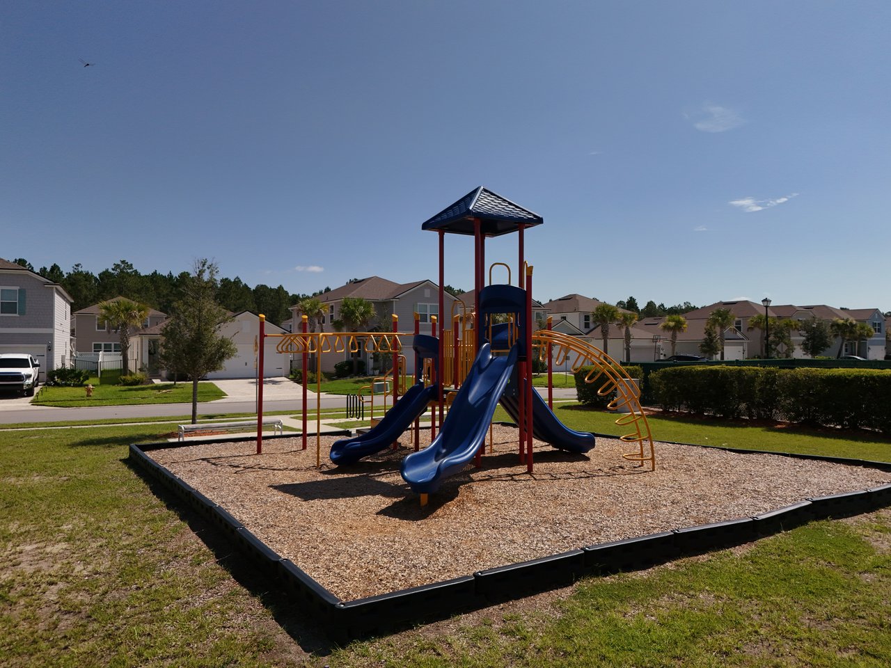 Community playground with blue slides and orange climbing equipment, surrounded by homes.