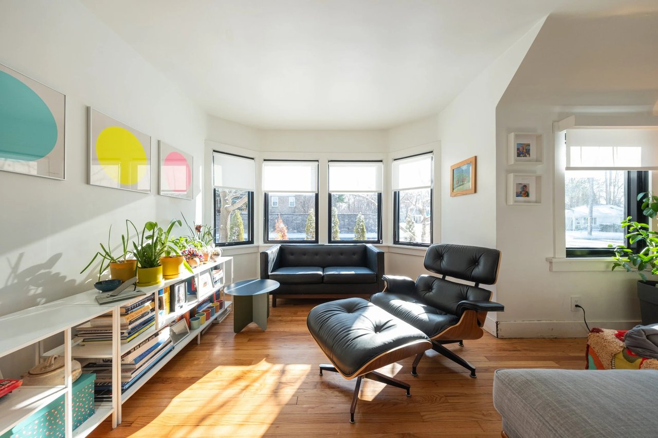 Living room with bay windows, hardwood floors, and a black leather lounge chair.