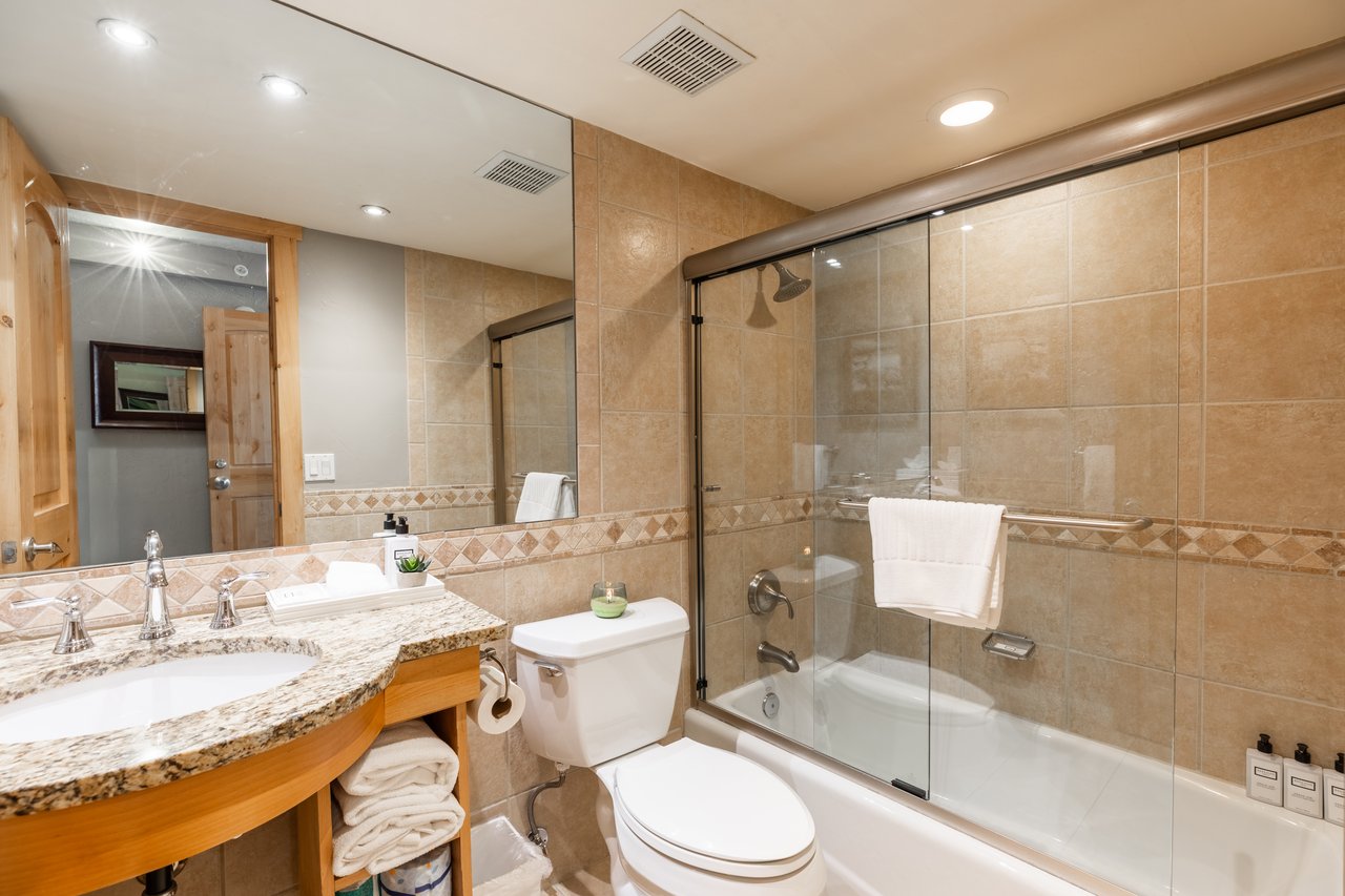 Condo bathroom with tan tile, glass-enclosed tub and shower, and granite vanity.