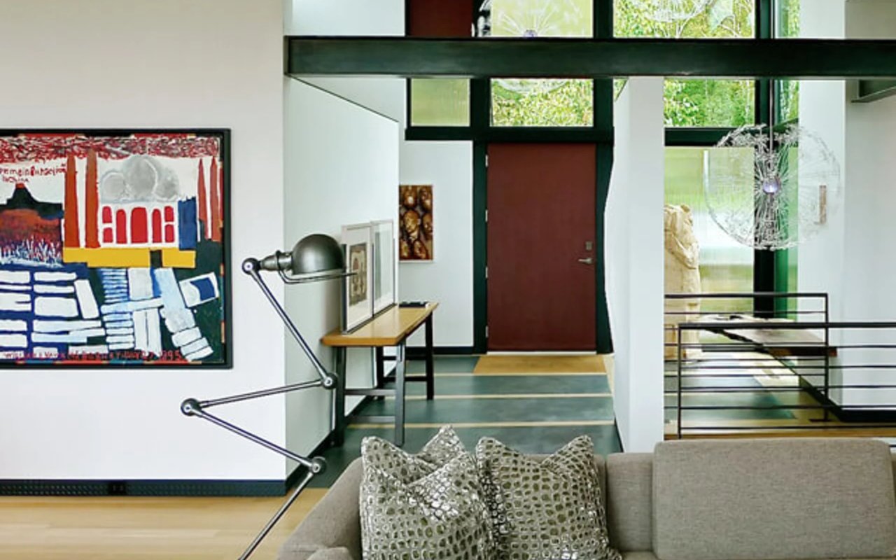Modern living room with abstract artwork, tall windows, and a red entry door.