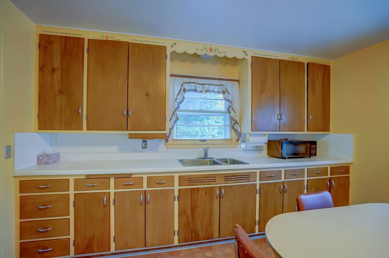 Kitchen with honey-colored cabinets, floral trim, and a double sink beneath the window.
