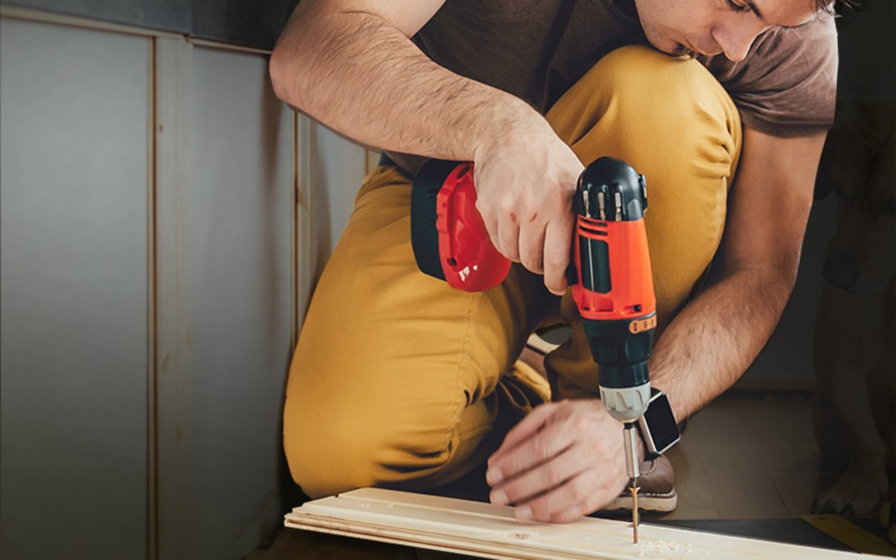 A man uses a cordless drill to fasten a wooden board during a home repair.