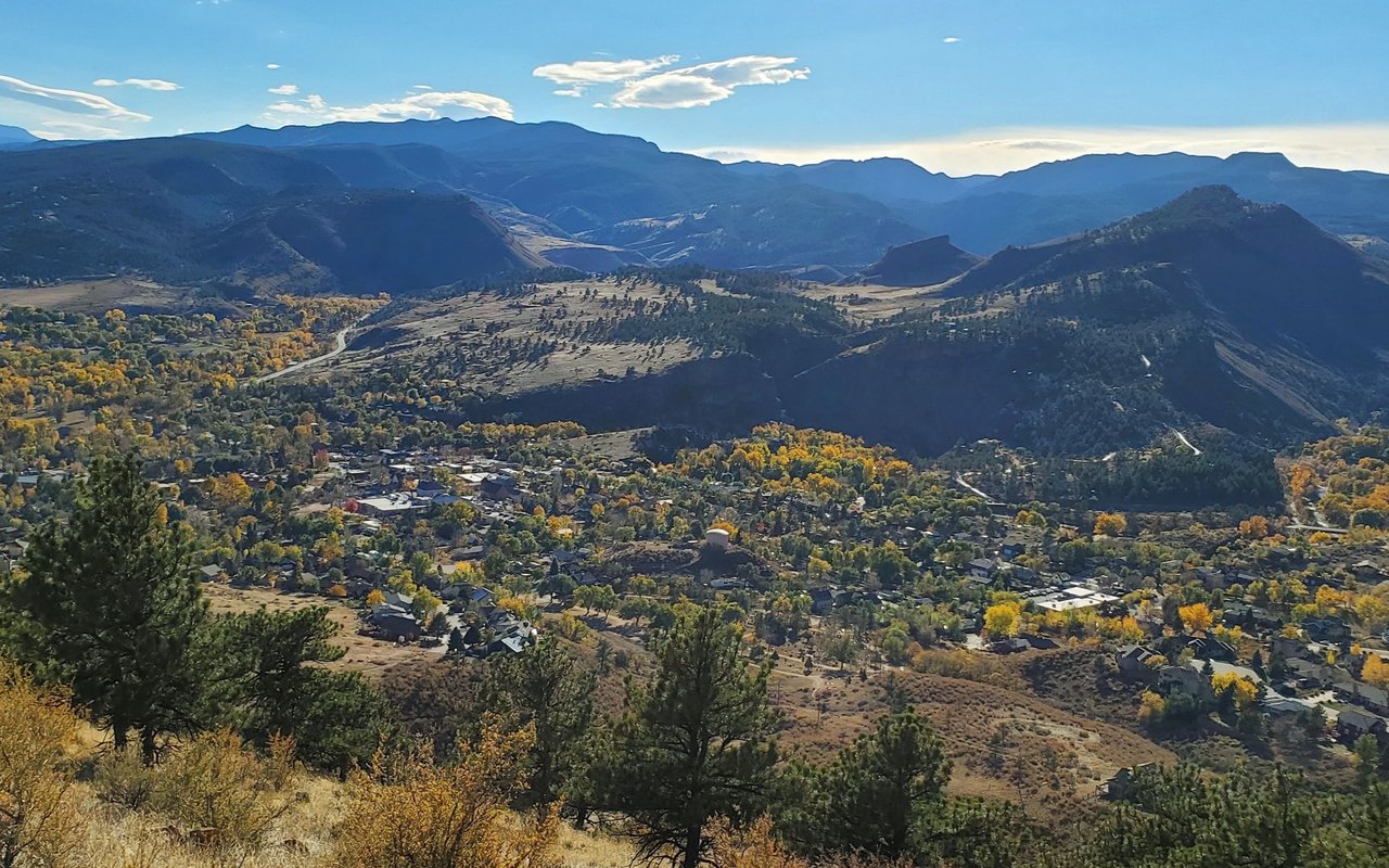 Mountain town nestled among autumn-colored foothills, with distant blue ranges beyond.