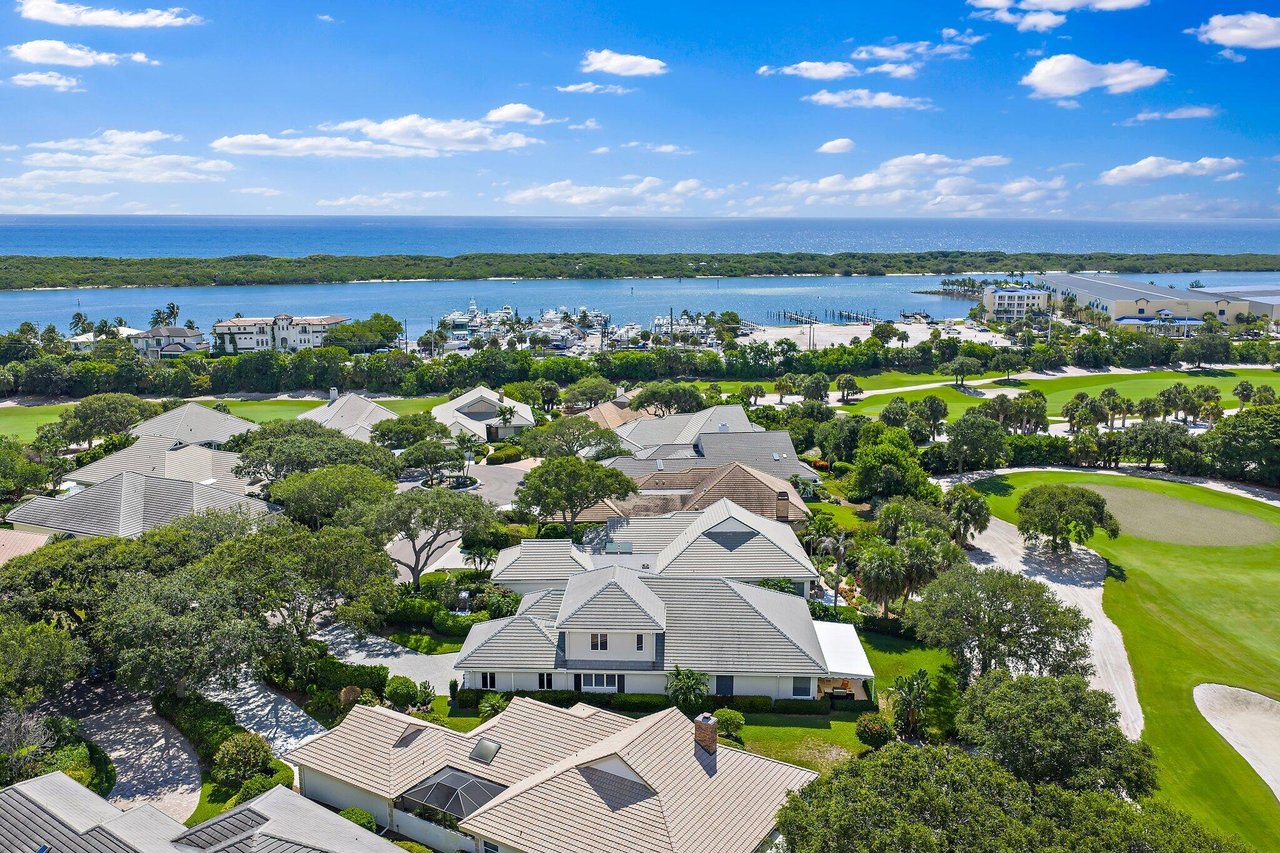 Aerial view of coastal homes beside a golf course, inlet, and ocean.