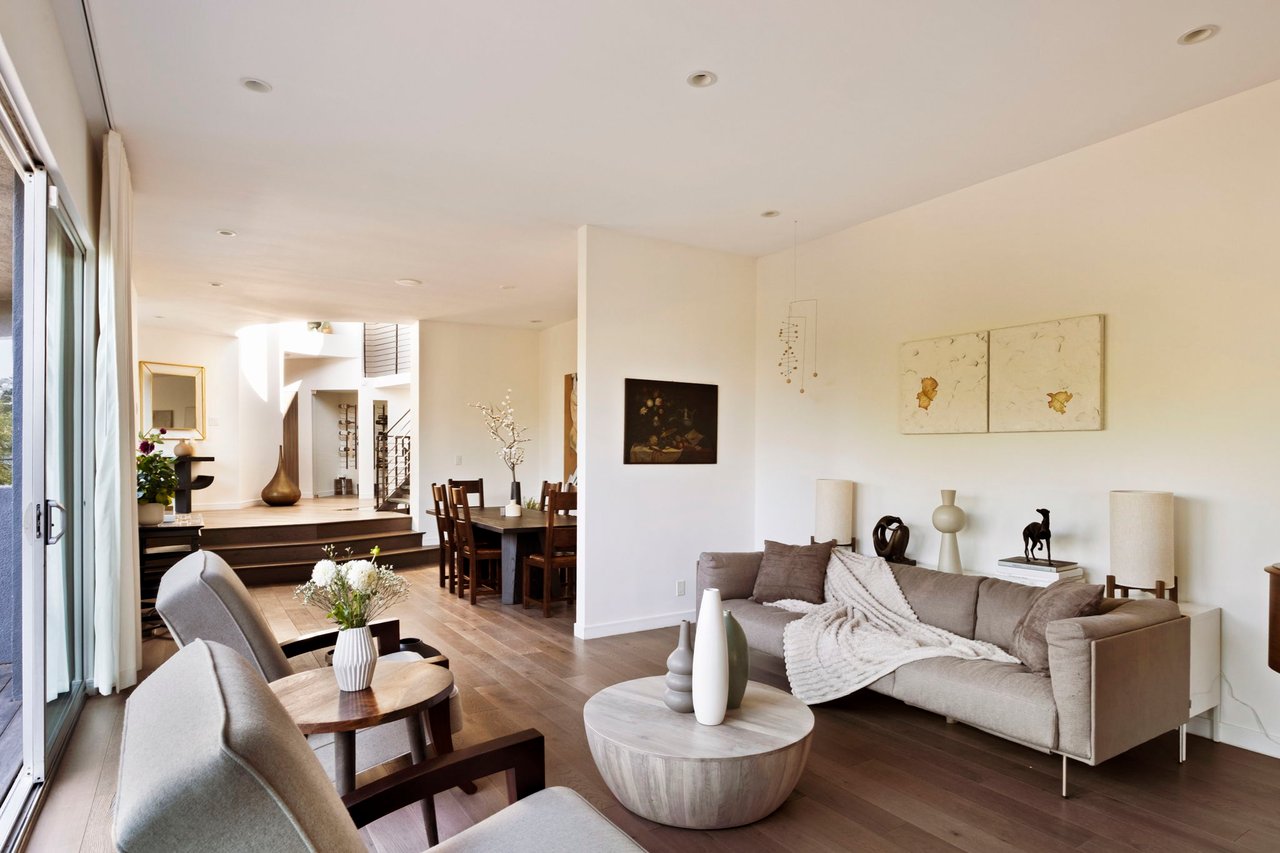 Open-plan living room with a neutral sectional, wood floors, and wide sliding glass doors.