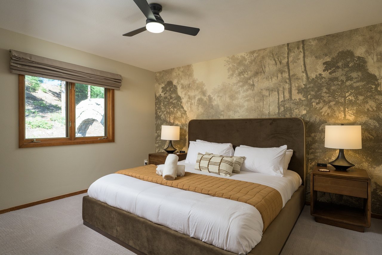 Bedroom with a sepia woodland mural behind a large bed and a window overlooking a stone arch.