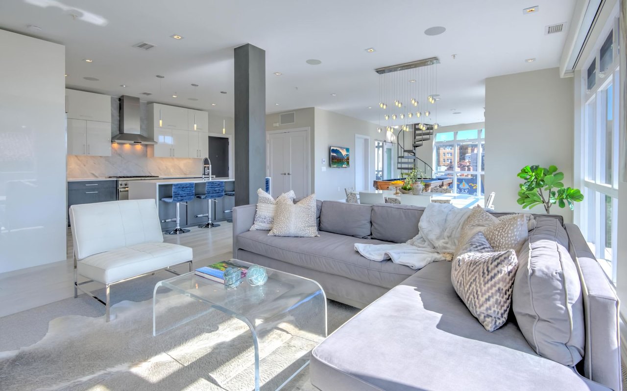 Modern open-concept living room and kitchen with gray sectional sofa, white armchair, and a marble kitchen island.