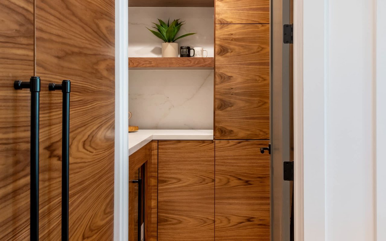 Built-in kitchen cabinetry with warm wood-grain fronts, black handles, and a white stone backsplash.