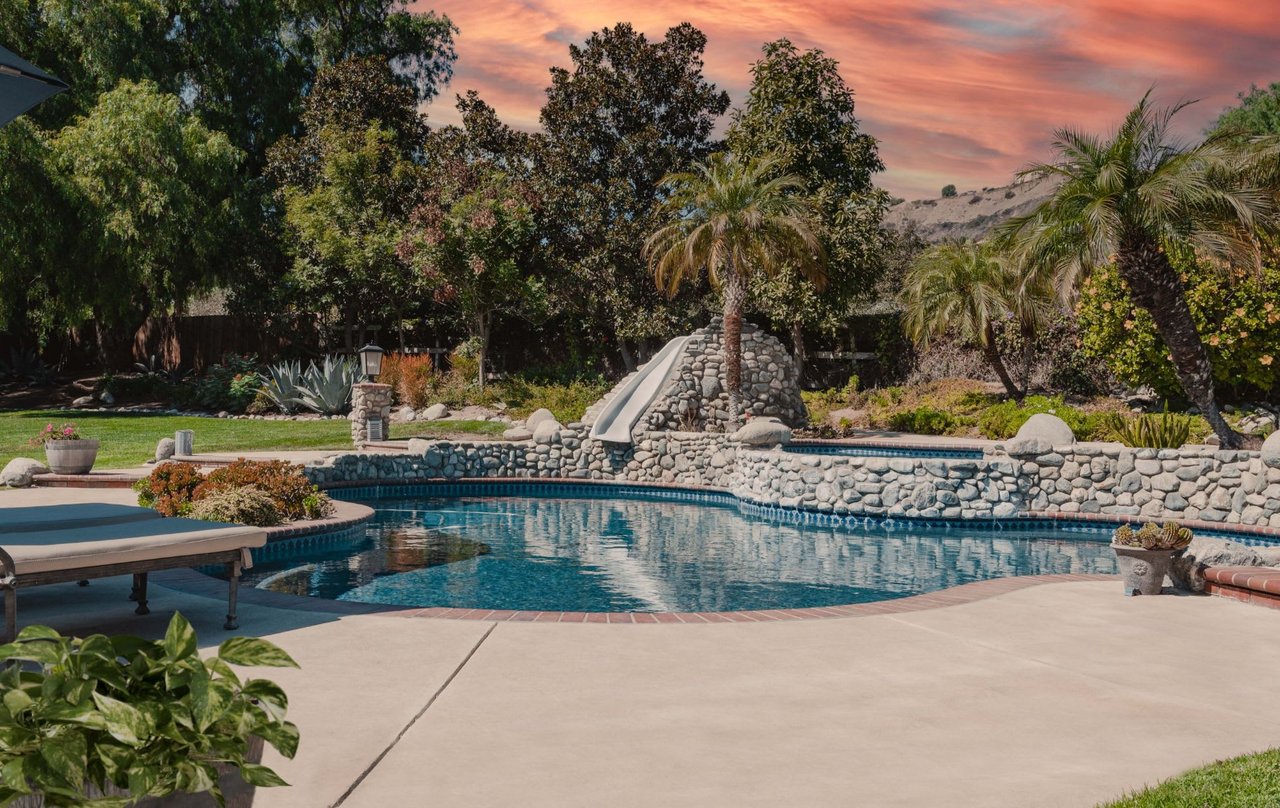  A resort-like backyard features a large, irregularly shaped swimming pool with a stone coping and a hot tub