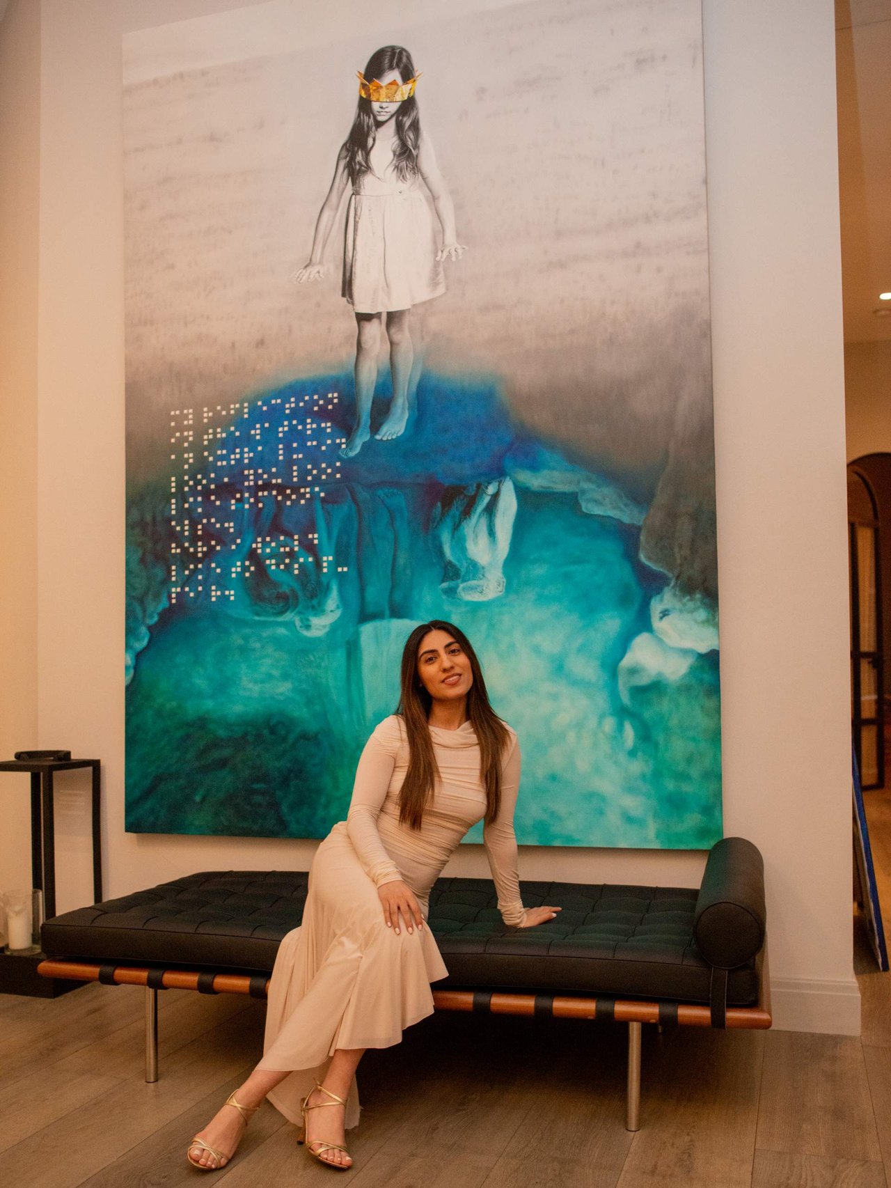 Woman in a cream dress seated on a black bench before a large turquoise artwork.