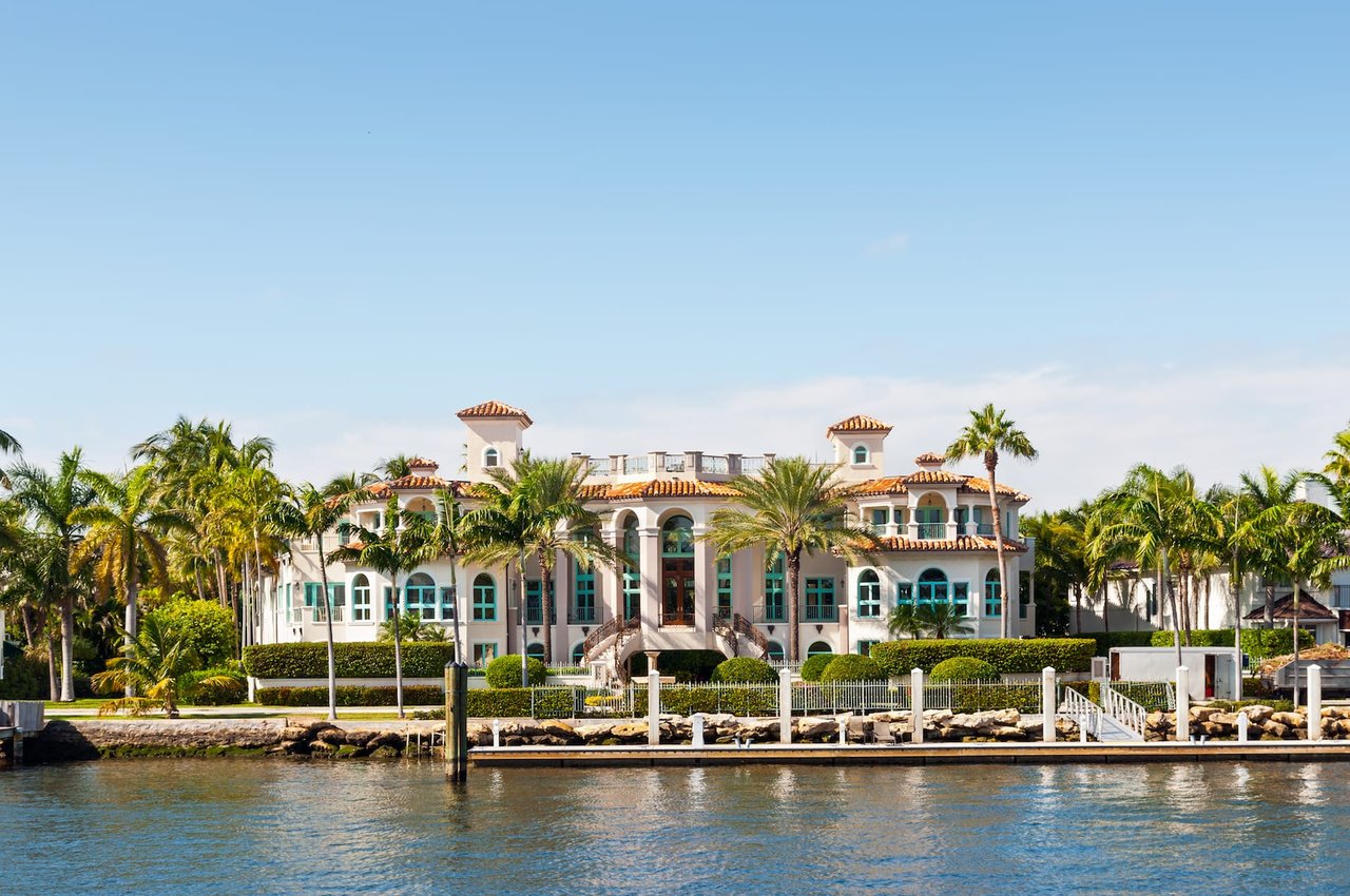  a large mansion surrounded by palm trees and a dock on a body of water