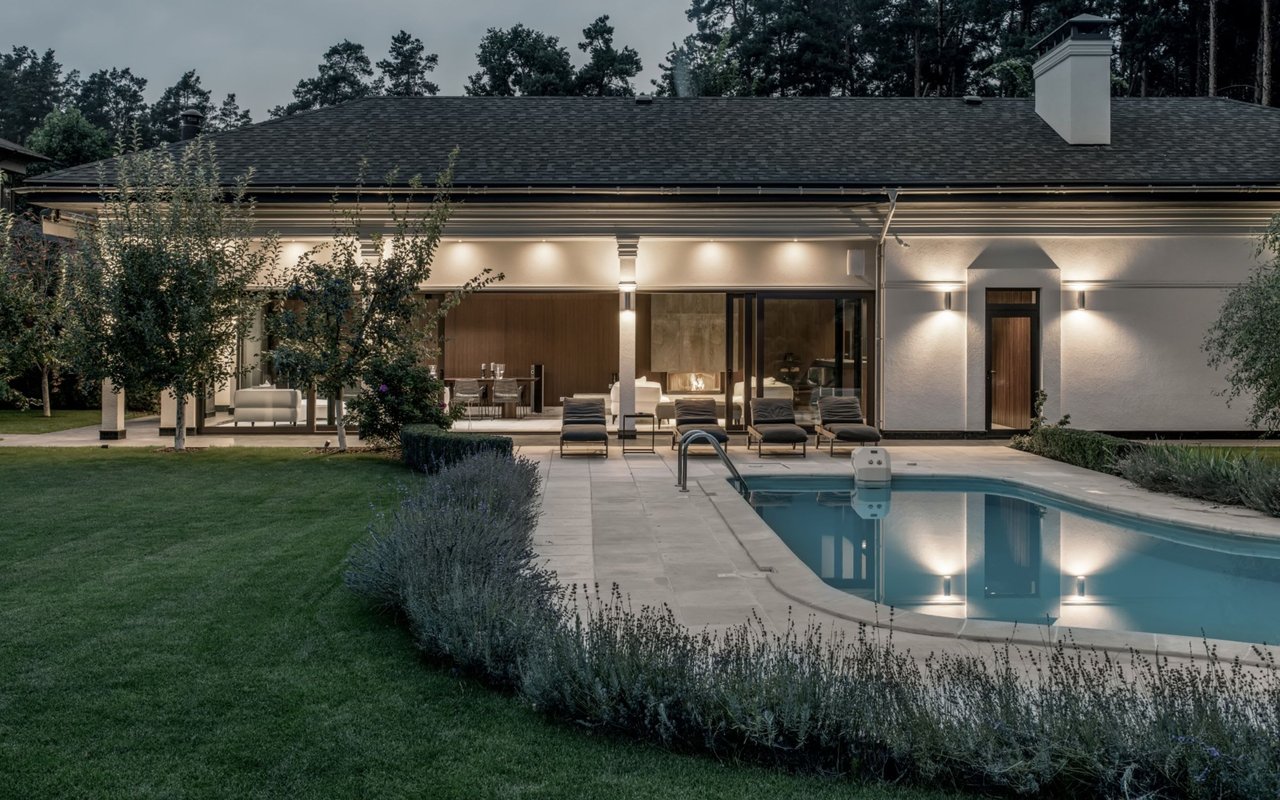 Modern home with an illuminated covered patio and swimming pool at dusk.
