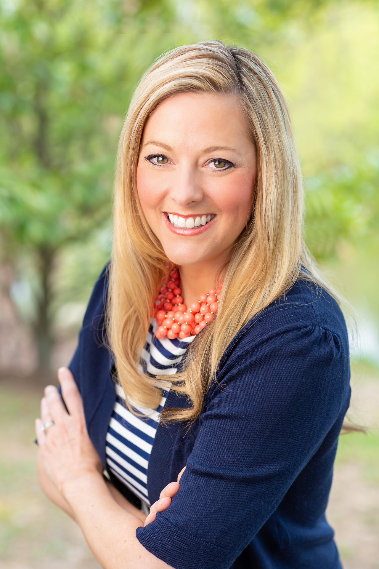Natalie Stephenson smiling with her arms crossed in a navy cardigan and coral necklaces