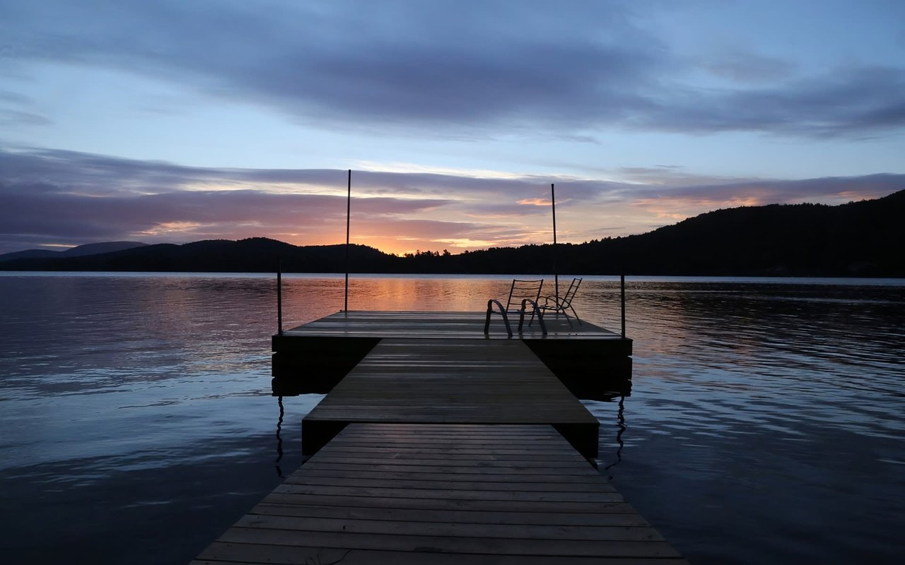  A wooden dock extends into a serene lake during sunset or sunrise