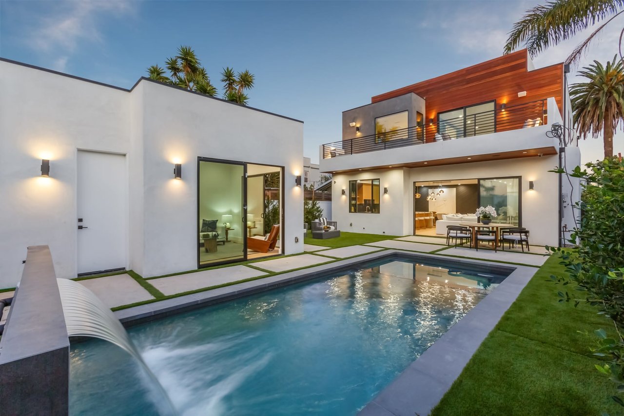 A sleek, modern outdoor living space features a rectangular swimming pool with a cascading water feature in the foreground.