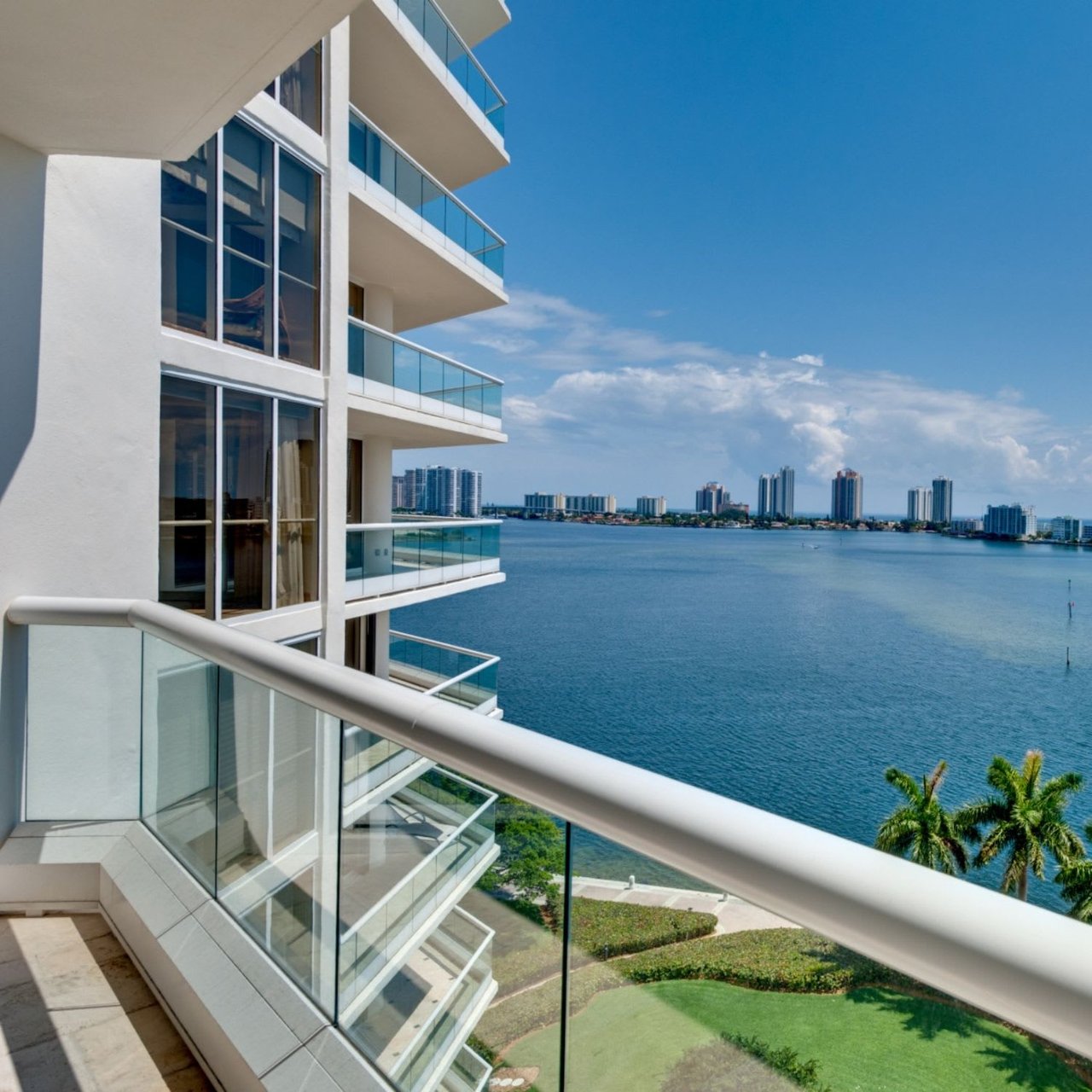  A high-angle view from a modern white building with glass balconies, overlooking a large expanse of deep blue water.