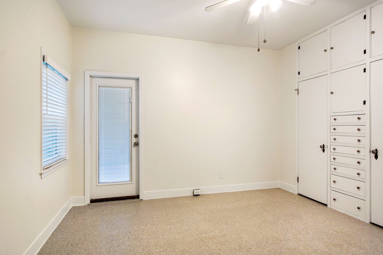 An interior shot of the primary bedroom, featuring built-in storage and a door leading outside. The room has a light color palette and ample natural light.