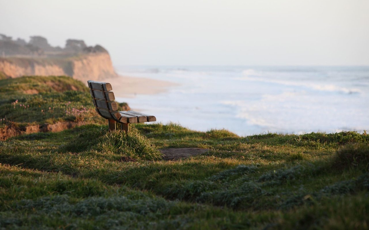 Wooden bench overlooking the Pacific Ocean from a grassy bluff in Half Moon Bay, California—offering stunning coastal views along the San Mateo County Coastside.