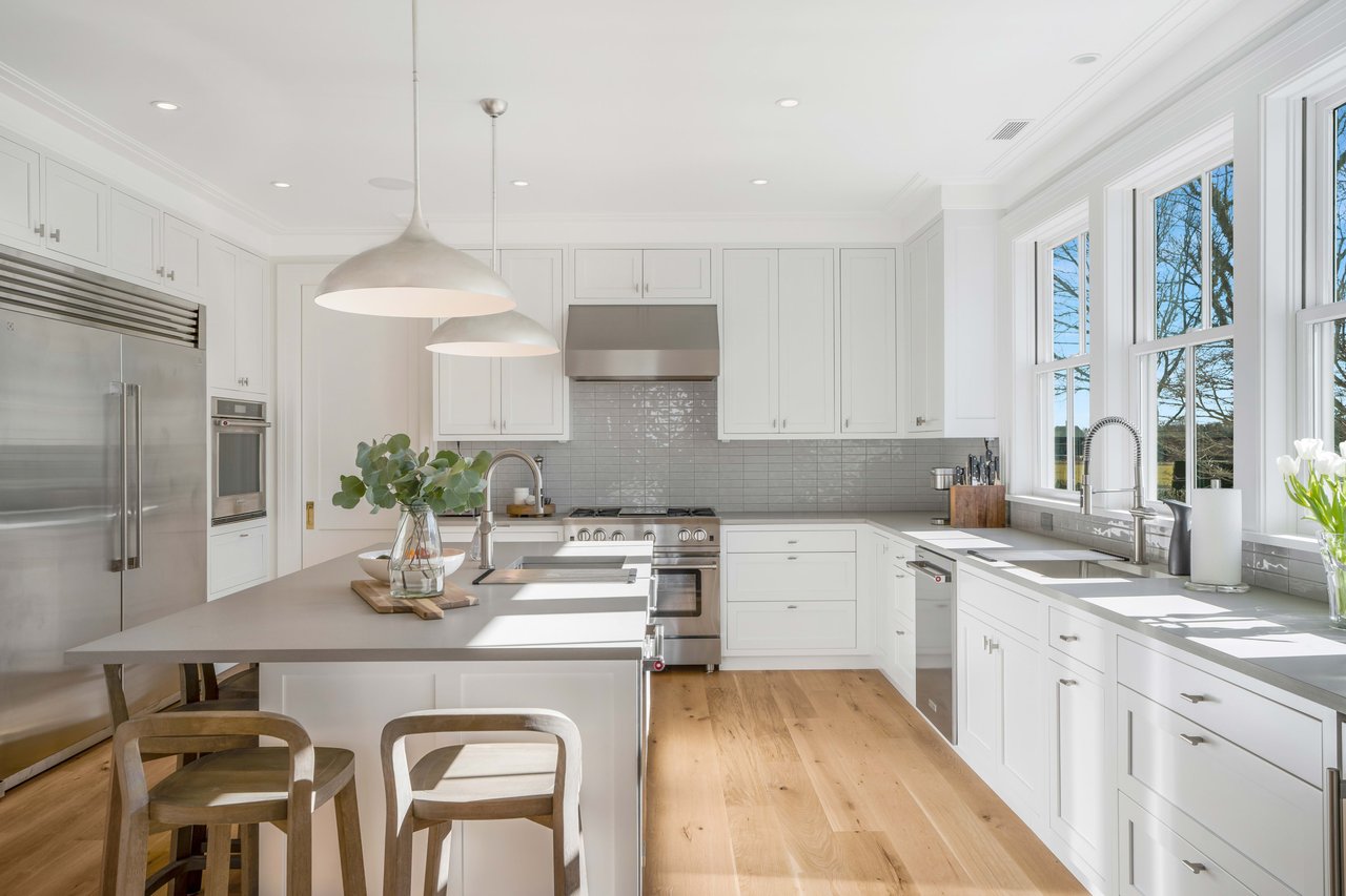 Modern kitchen with white cabinets, stainless steel appliances, and wooden floors.