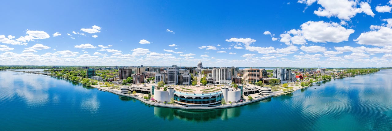Aerial panorama of downtown Madison along the lake, with Monona Terrace and the Wisconsin State Capitol.