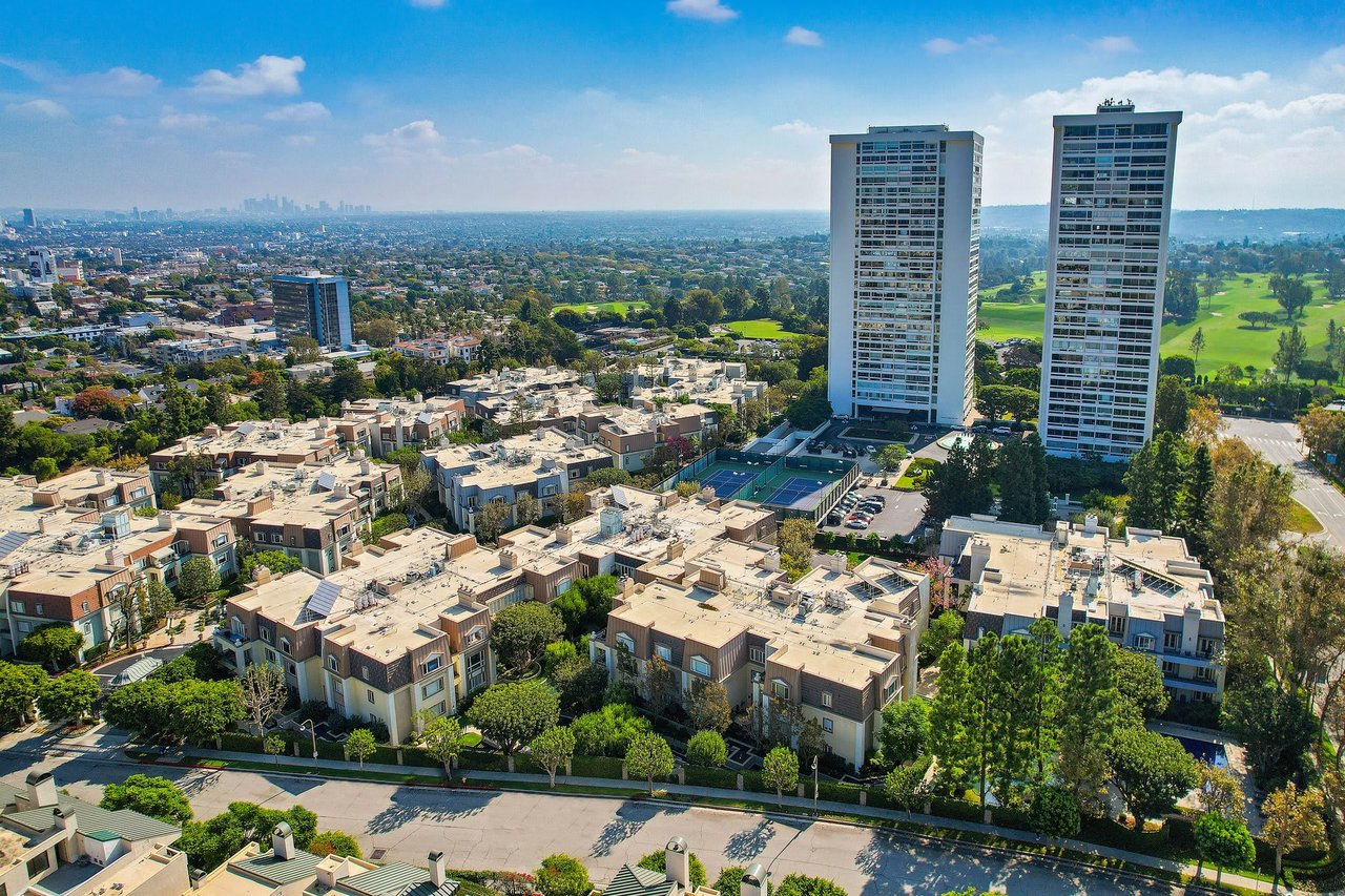There are numerous low-rise residential buildings with light-colored facades and darker roofs, interspersed with green trees and landscaping.
