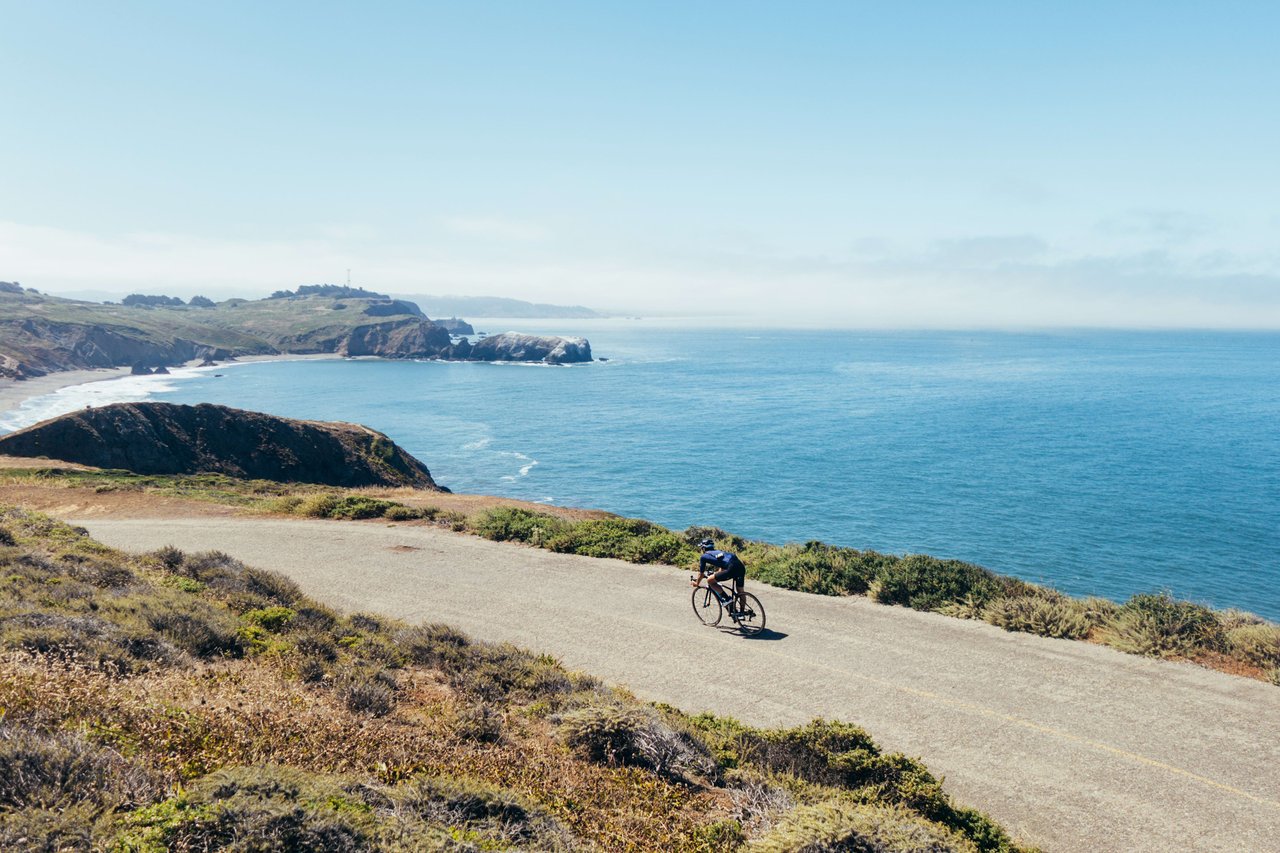 A person on a bicycle rides on a dirt path along the coast.