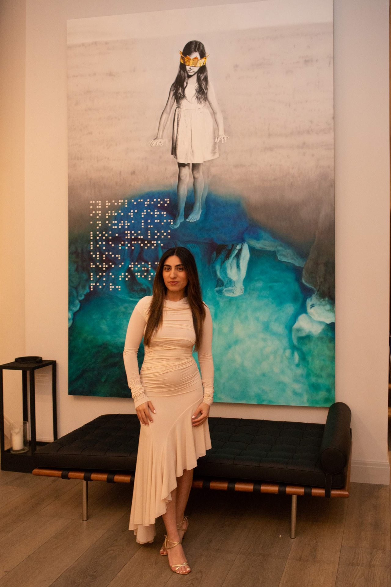 Woman in a pale blush dress standing before a large blue-toned artwork in a lounge.