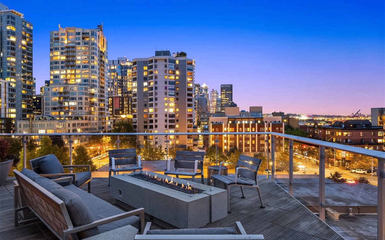  An outdoor rooftop patio at dusk offers a panoramic view of a city skyline.