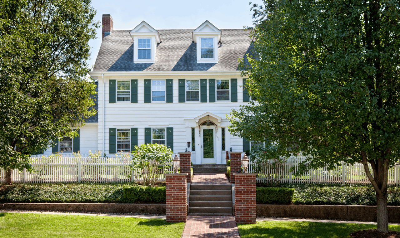 A white house with green shutters and a white picket fence.