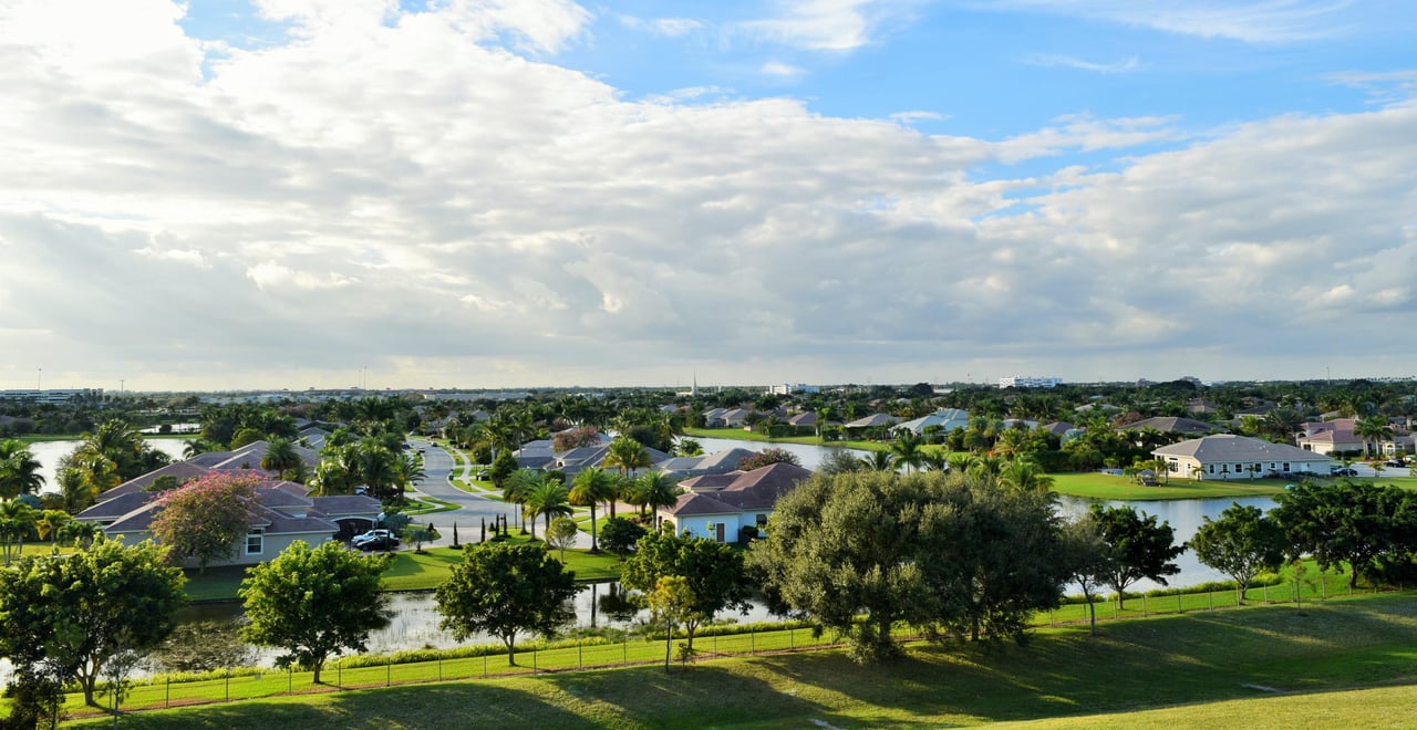 Serene aerial view of suburban homes with red and brown roofs amid green lawns and winding streets.