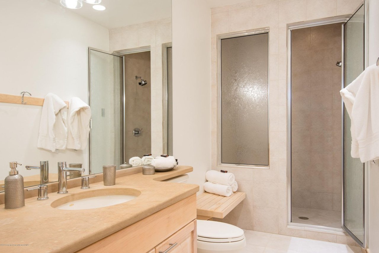 Bathroom with a pale stone vanity, mirrored wall, and two glass-enclosed shower areas.