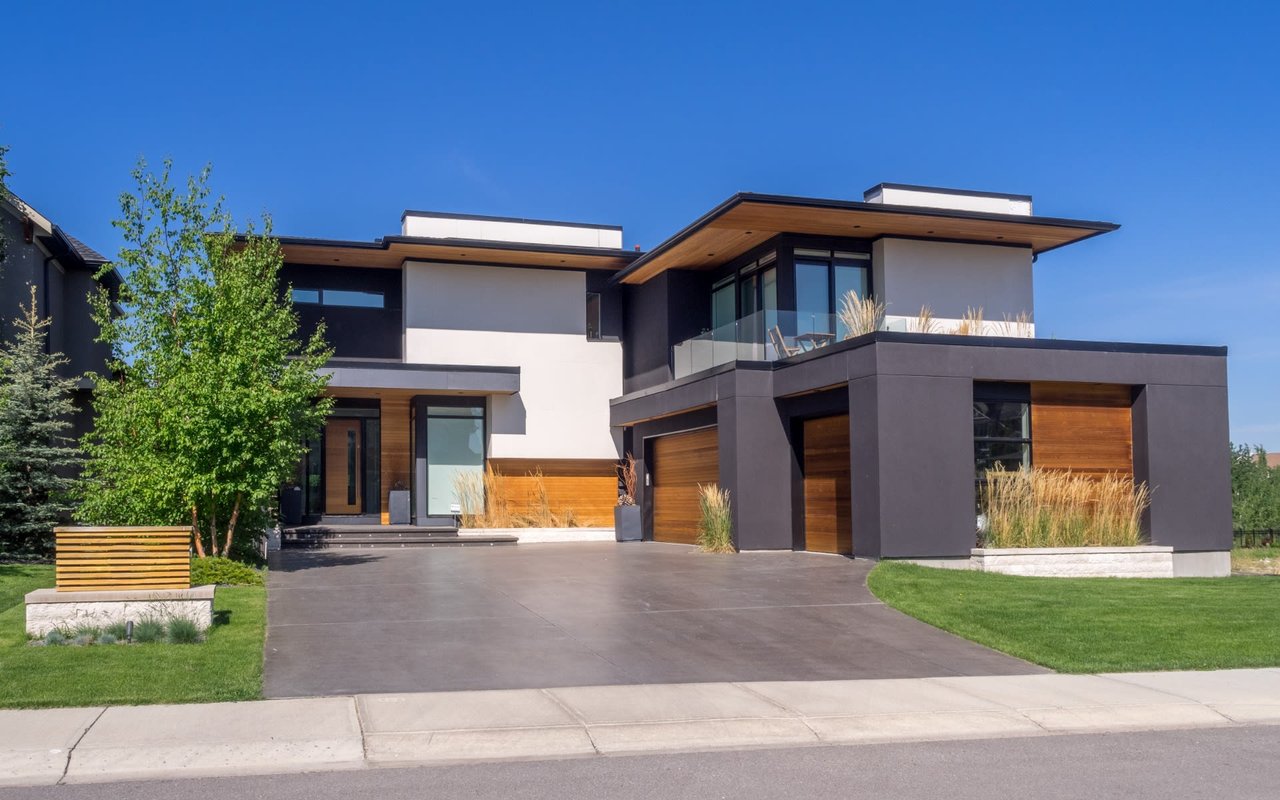 A contemporary multi-story house with a flat roof, featuring a facade of dark gray, white, and natural wood panels.