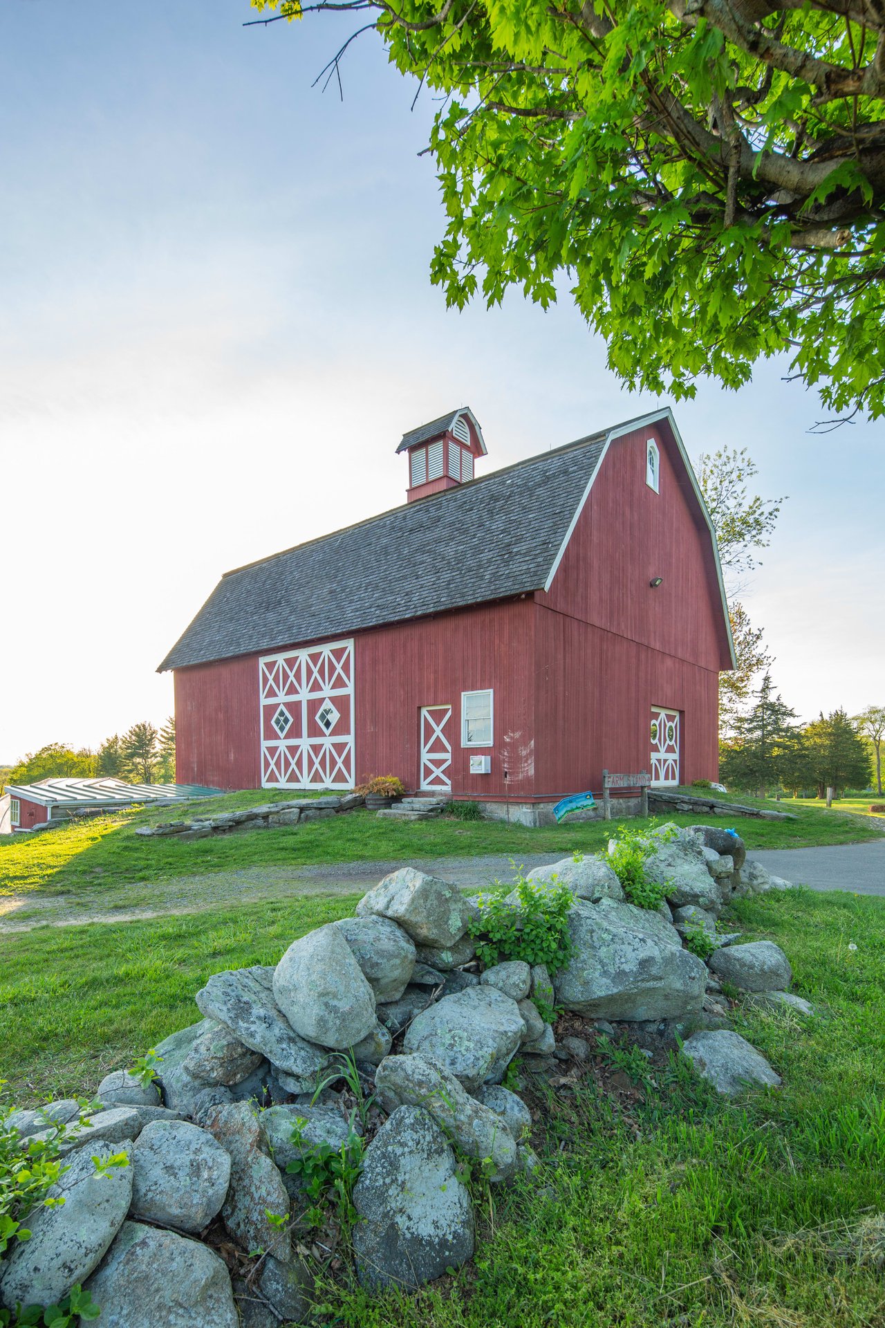 A red barn with a grey roof and trim, sitting next to a stone wall.