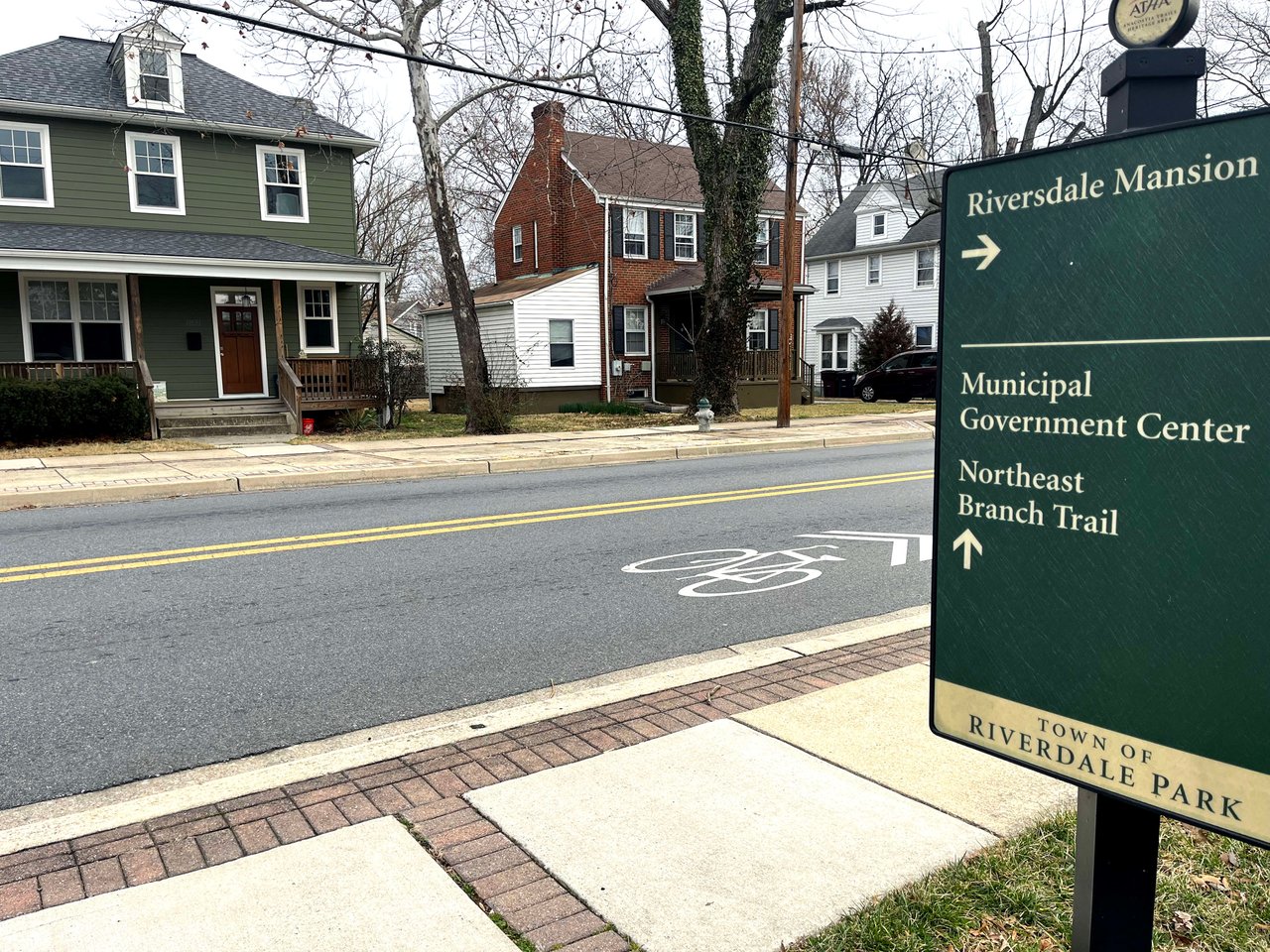  A street scene in the "Town of Riverdale Park" with a dark green directional sign in the foreground on the right.