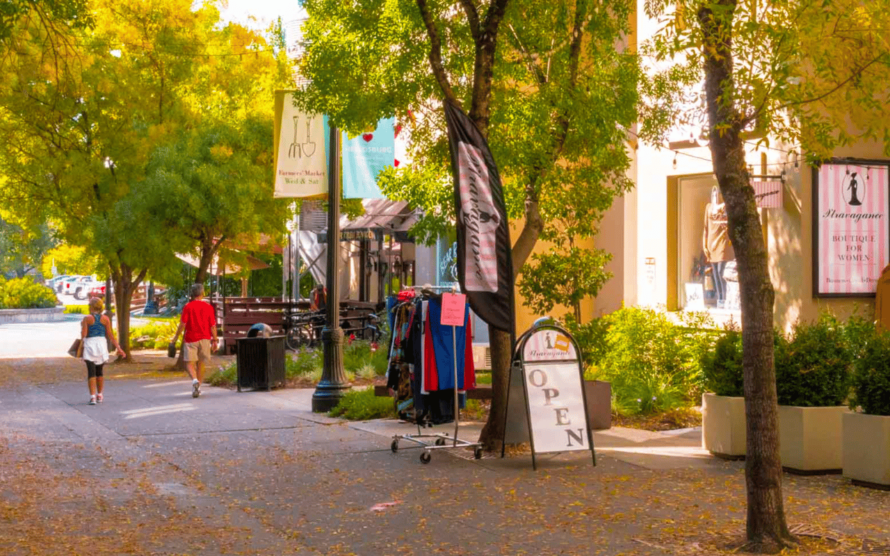 Two people walking beside a storefront with a large open sign and clothes hanger.