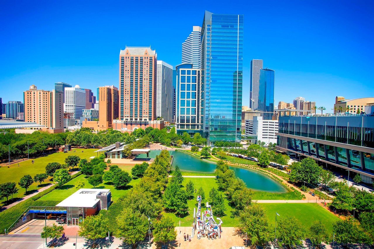 Downtown Houston skyline above a green park and pond, with a colorful sculpture in the foreground.