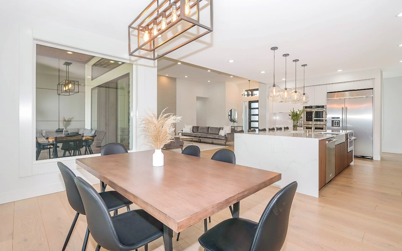 Bright, modern dining room, wood table, black chairs, pendant lights, open concept with kitchen, living room view.