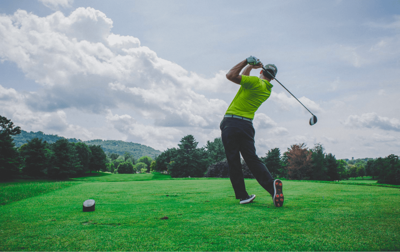 A man in a green shirt playing golf under clear skies.