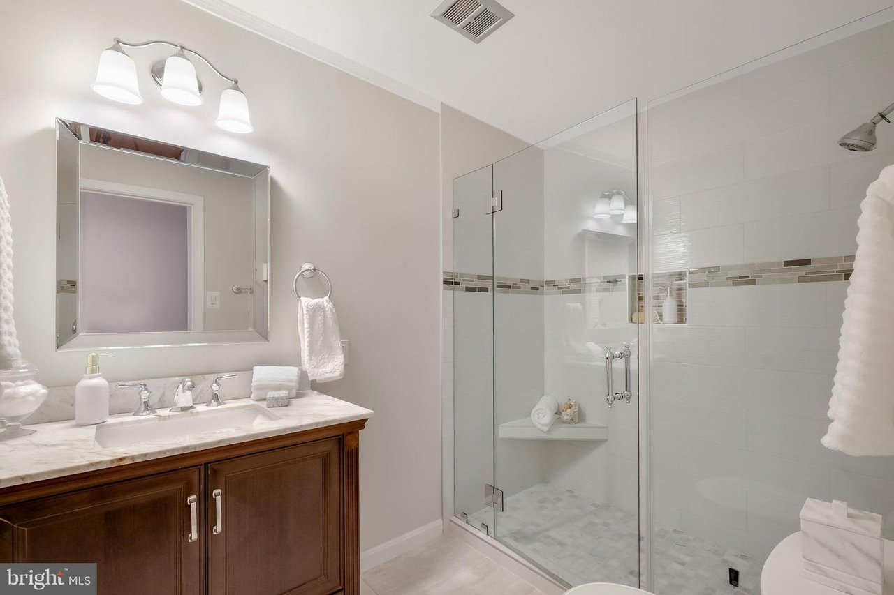 Bathroom with a dark wood vanity and glass-enclosed shower featuring a mosaic tile accent band.