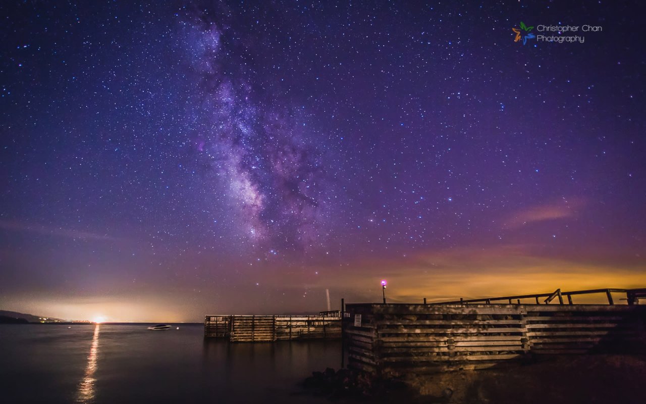 Stunning night sky with the Milky Way galaxy, illuminated by a distant light on a calm lake.