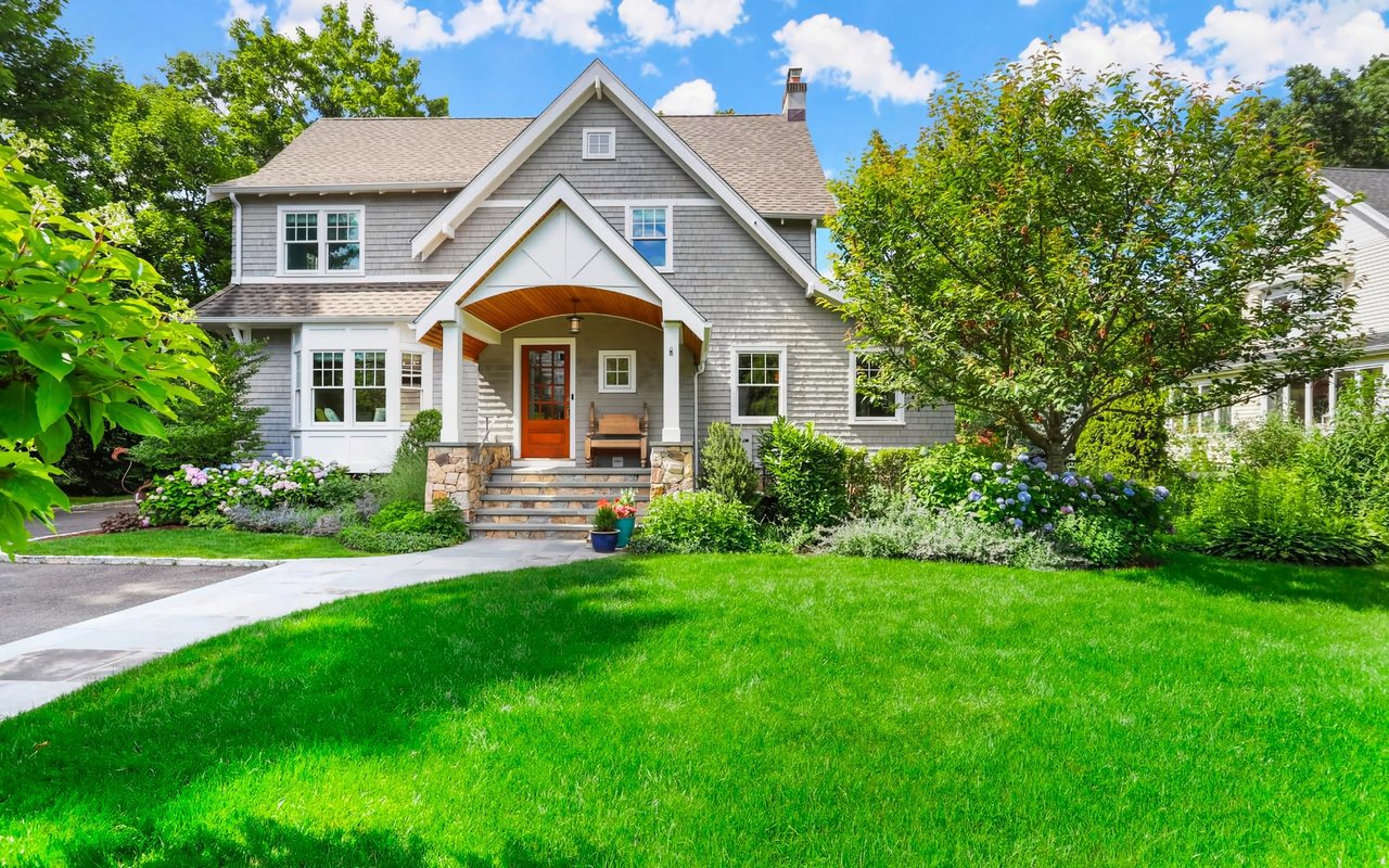 A large two-story colonial-style home with a white exterior, a picket fence, a front yard, and a paved driveway.