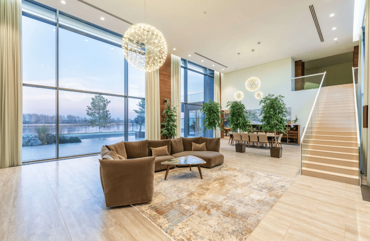 Spacious living room with couch, table, stairs, glass wall, and light tones