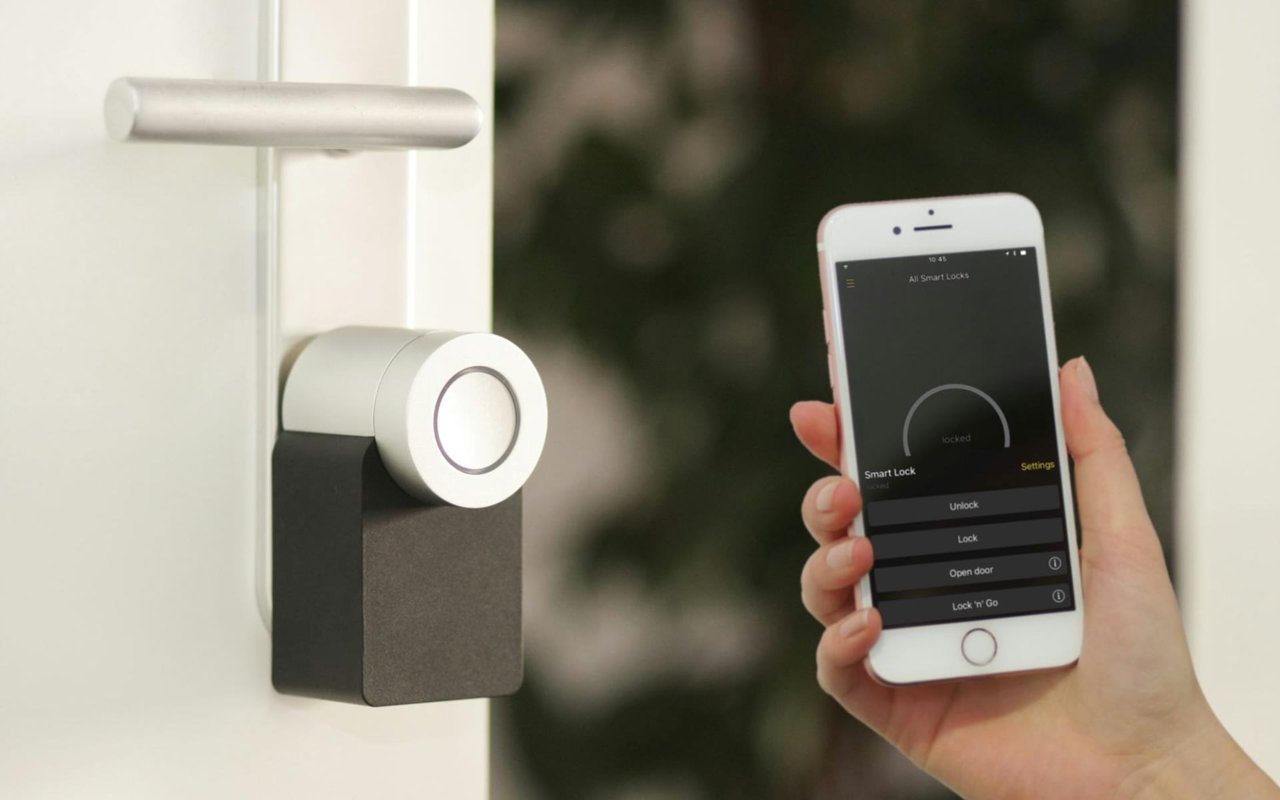 A person holding a smartphone next to a smart lock on a door.