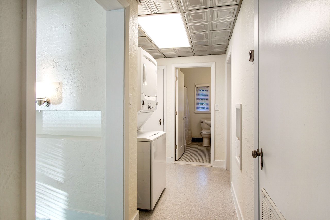 A hallway in a home, leading to different rooms. The hallway is well-lit, with modern decor and possibly a utility area visible.