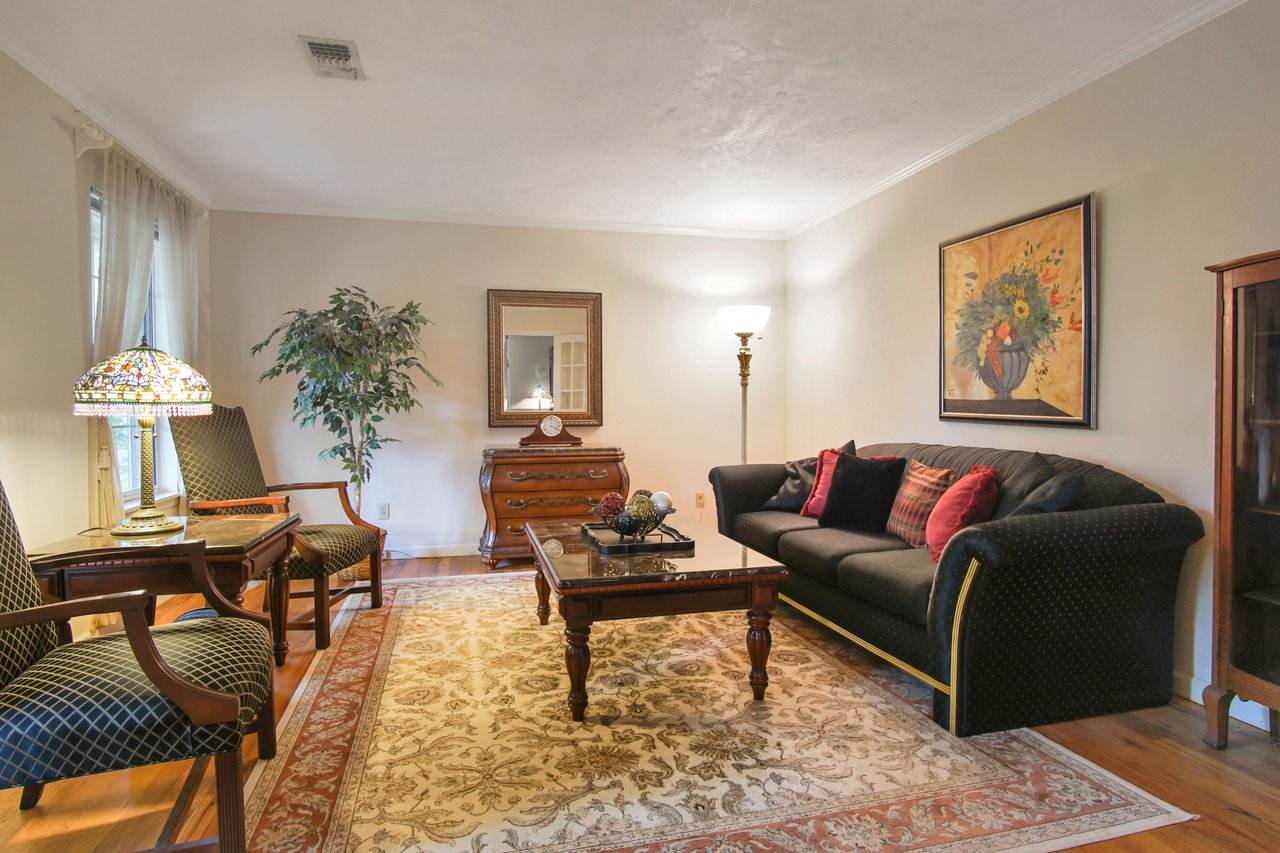 A living room with comfortable seating, including sofas and armchairs. The room is decorated with artwork, rugs, and plants, creating a cozy atmosphere.